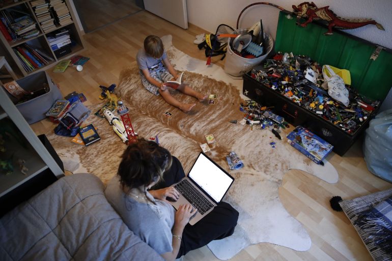 A Woman Works At A Laptop Computer On The Floor Of A Bedroom As A Child Sits Alongside Reading A Book In This Arranged Photograph Taken In Bern, Switzerland, On Saturday, Aug. 22, 2020. The Biggest Wall Street Firms Are Navigating How And When To Bring Employees Safely Back To Office Buildings In Global Financial Hubs, After Lockdowns To Address The Covid-19 Pandemic Forced Them To Do Their Jobs Remotely For Months. Photographer: Stefan Wermuth/Bloomberg